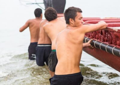 Voyage incentive en Nouvelle-Zélande : Hommes maoris entrant un grand waka rouge dans la mer aux Waitangi Treaty Grounds, Nouvelle-Zélande