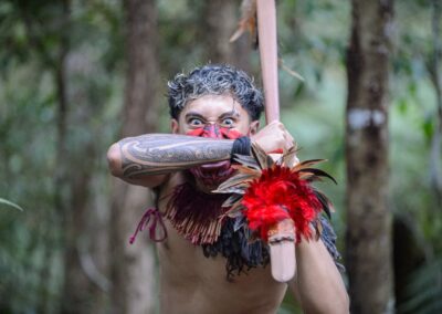 Learning-trip en Nouvelle-Zélande : Guerrier maori en forêt, tenant une arme traditionnelle, tatouage moko sur le bras