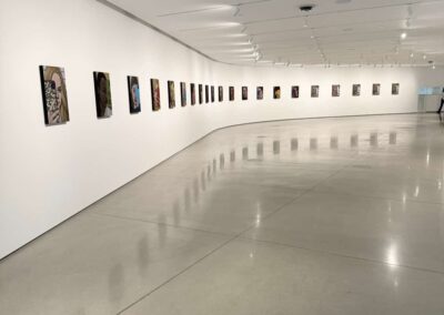 Voyage Incentive en Californie : Salle d’exposition lumineuse où sont exposées les « Nice girl » 21 portraits d’Amy Adler au musée OCMA à Costa Mesa avec œuvres accrochées et visiteurs dans l’espace.