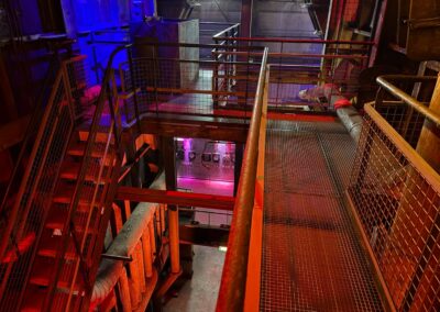 Voyage en famille dans les Vosges : Passerelles dans la centrale de Wesserling, éclairés par des lumières violettes, jaunes, rouges et bleues.