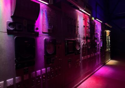 Voyage sur mesure dans les Vosges : Panneaux de commande et instruments industriels dans la centrale de Wesserling, éclairés par des lumières violettes.