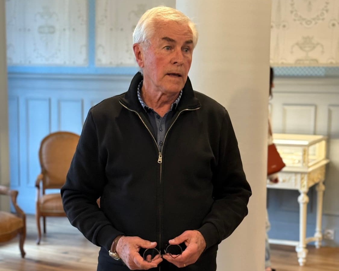 Séjour familial en Auvergne : Serge Teillot, propriétaire de Subirana s'exprime devant un groupe de visiteurs dans un salon d'époque de la Maison Rozier, tenant deux petits objets ronds dans ses mains.