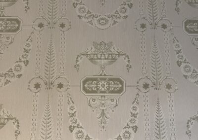 Séminaire original en Auvergne : Gros plan sur un papier peint ancien à motifs néoclassiques dorés, urnes, guirlandes de fleurs et fougères stylisées (Maison Rozier)