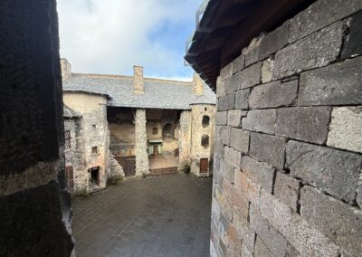 Escapade entre amis en Auvergne : Cour intérieure pavée du château de Murol bordée de bâtiments en pierre et galerie en bois.