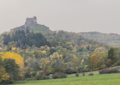 Voyage sur mesure en Auvergne : Château de Murol perché sur son piton volcanique, vu de loin dans la brume automnale.