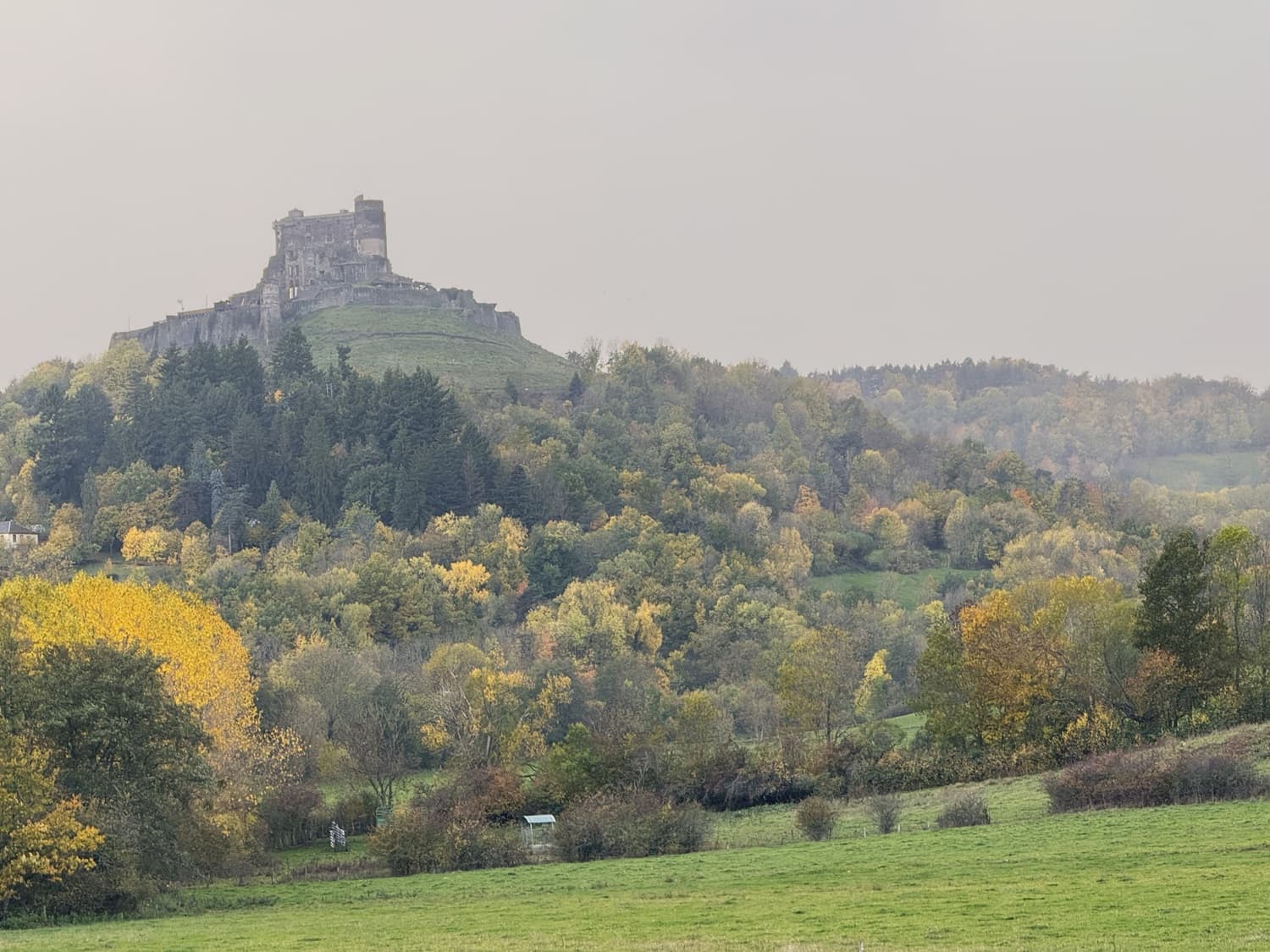 Le château de Murol dominant la vallée. Voyage sur mesure en Auvergne : Château de Murol perché sur son piton volcanique, vu de loin dans la brume automnale.
