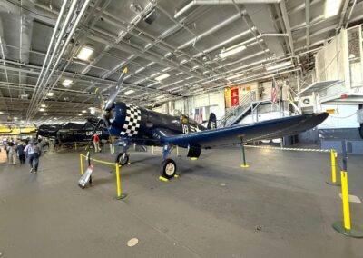 Séminaire à Los Angeles : Avion de chasse « F4U Corsair » bleu marine au nez à damier, exposé sur le pont hangar de l'USS Midway parmi d'autres appareils historiques (San Diego).