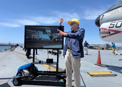 Voyage exclusif entre amis en Californie : Guide bénévole vétéran de la Navy commentant devant un écran les manœuvres du pont d'envol, à côté d'un avion » A-7 Corsair II » exposé sur l'USS Midway (San Diego).