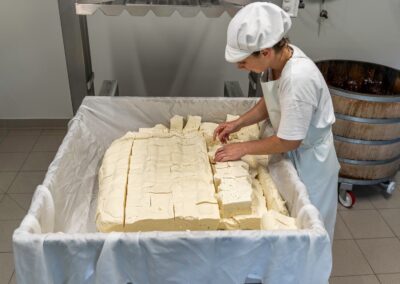 Voyage gastronomique en Auvergne : Fromagère découpant et retournant les blocs de tome pressée pour la fabrication du Cantal ou du Salers.