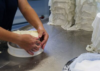 Visite hors des sentiers battus en Auvergne : Fromagère enveloppant un fromage salé dans un linge, entouré de toiles superposées d'autres fromages en égouttage, fabrication du Saint-Nectaire.