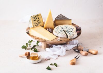Séjour familial en Auvergne : Assortiment de 5 fromages AOP Auvergne sur un plateau sur pied en bois avec miel, noix, couteaux et fond texturé.
