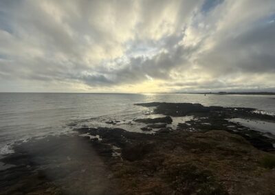 Voyage sur mesure en Bretagne : Rochers noirs à marée basse face à l'océan sous un ciel nuageux, sur la côte du domaine de Rochevilaine dans le Morbihan.