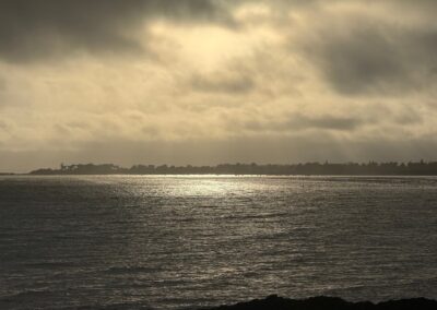 Séjour luxe familial en Bretagne : Reflets de lumière sur la mer sous un ciel orageux, avec la côte bretonne en silhouette à l'horizon, vue depuis Rochevilaine.
